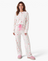 Beach Rose Co. woman wearing a cream pajama set with pastel Christmas diamond print, Henley top, and pink ribbon tie.
