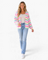 Beach Rose Co. model wearing a pink and pastel rainbow striped open-front knit cardigan with jeans and white sneakers.