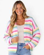 Beach Rose Co. model wearing a pink and pastel rainbow striped open-front knit cardigan with long dropped sleeves.