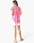 Beach Rose Co. pink abstract animal print V-neck top with cuffed sleeves and back pleat, worn with white shorts.