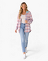 Beach Rose Co. pink and blue plaid shacket with a cream sherpa collar, worn by a smiling model with jeans and sneakers