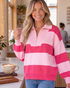 Beach Rose Co. pink and fuchsia striped half-zip sweater with balloon sleeves worn by a smiling woman in a cafe.