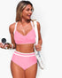 Beach Rose Co. pink high-waisted bikini with cross-front top and white trim, worn by a woman with a white mesh bag.