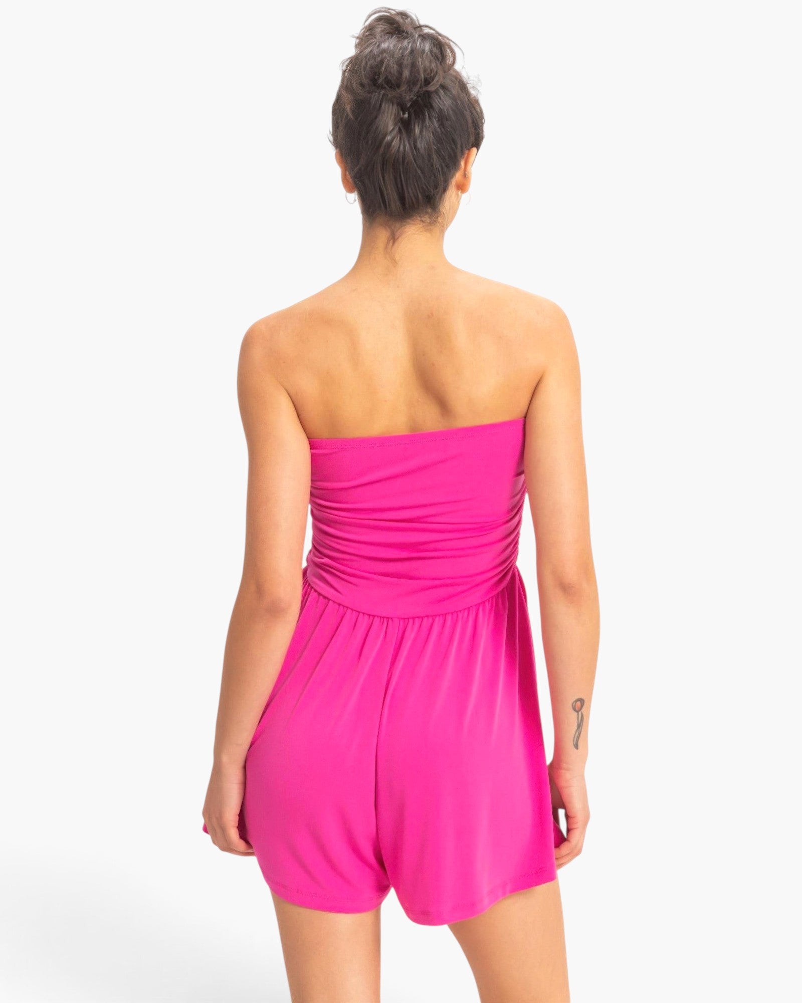 Back view of a model wearing a Beach Rose Co. hot pink strapless romper with shirred waist and relaxed shorts