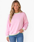 Beach Rose Co. pink crewneck sweatshirt with green and white striped ribbed trim on a model wearing blue jeans.