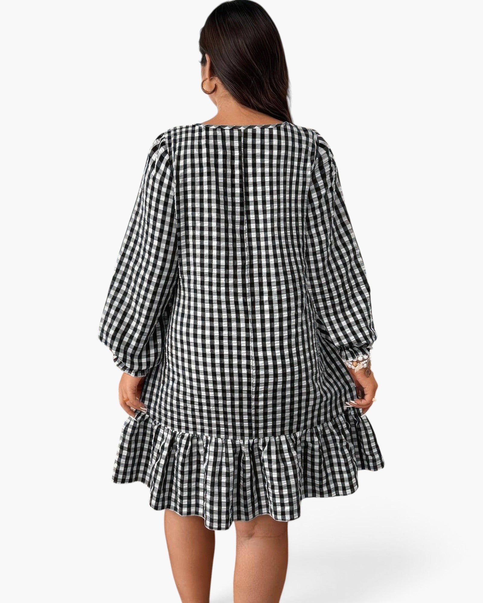 A woman viewed from the back wearing a black and white gingham mini dress with long balloon sleeves and a ruffled hem, against a plain light gray studio background.