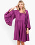 Beach Rose Co. plum babydoll dress with tiered bell sleeves, gathered neckline, and tie detail on a smiling model.