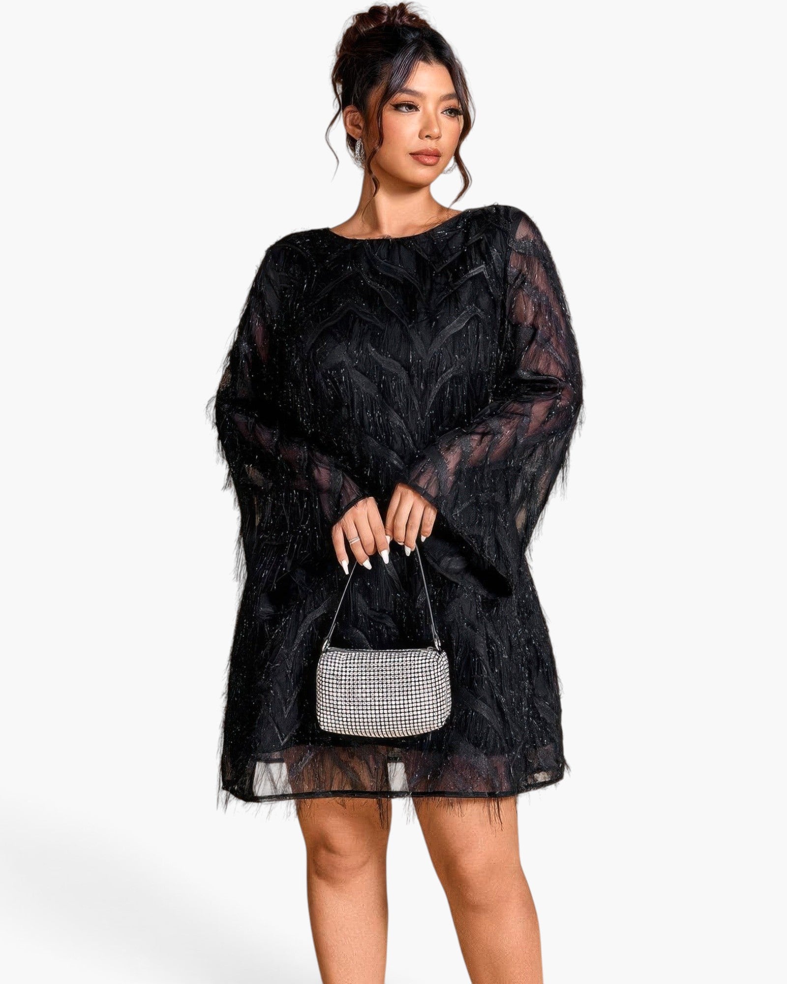 A woman modeling a black sheer lace mini dress with textured feather-like embroidery and long balloon sleeves, holding a small rhinestone-embellished handbag against a plain light gray studio background.