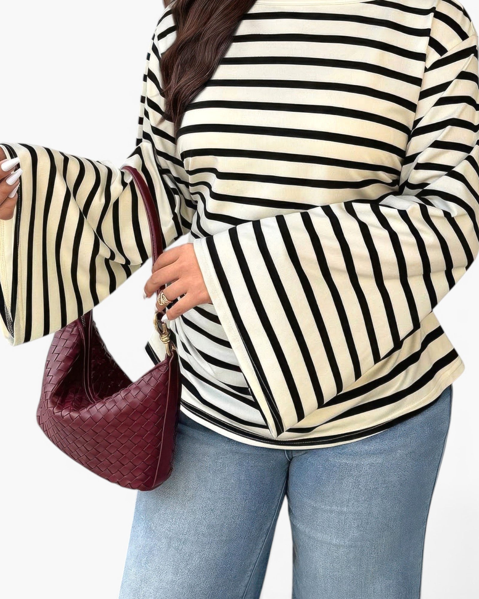 A person wearing a cream and black horizontally striped long-sleeve top with wide flared sleeves, paired with light blue jeans and carrying a burgundy woven shoulder bag.