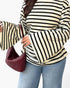 A person wearing a cream and black horizontally striped long-sleeve top with wide flared sleeves, paired with light blue jeans and carrying a burgundy woven shoulder bag.