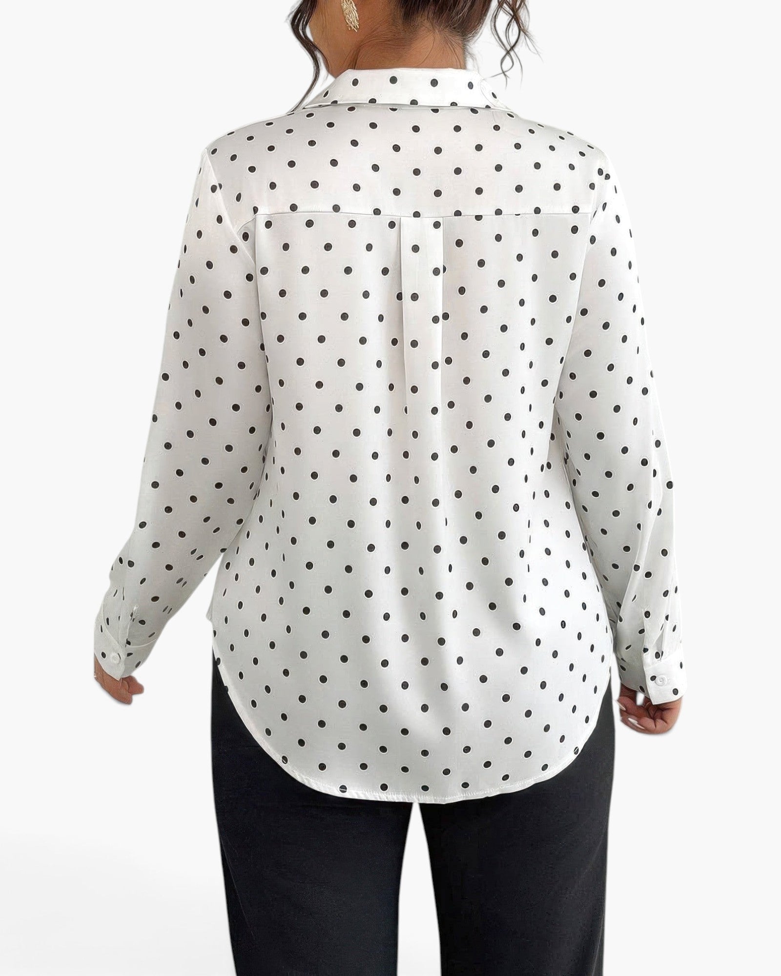 A woman shown from the back wearing a white long-sleeve blouse with a black polka dot pattern and black pants, against a plain white studio background.