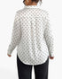 A woman shown from the back wearing a white long-sleeve blouse with a black polka dot pattern and black pants, against a plain white studio background.