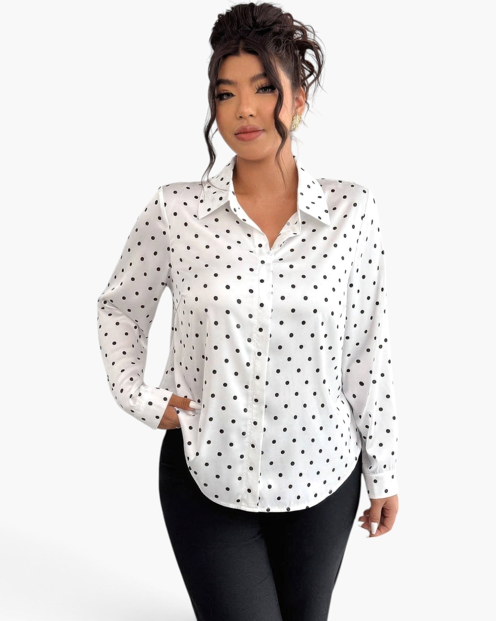 A woman modeling a white long-sleeve button-up blouse with a black polka dot pattern, paired with black pants, against a plain white studio background.