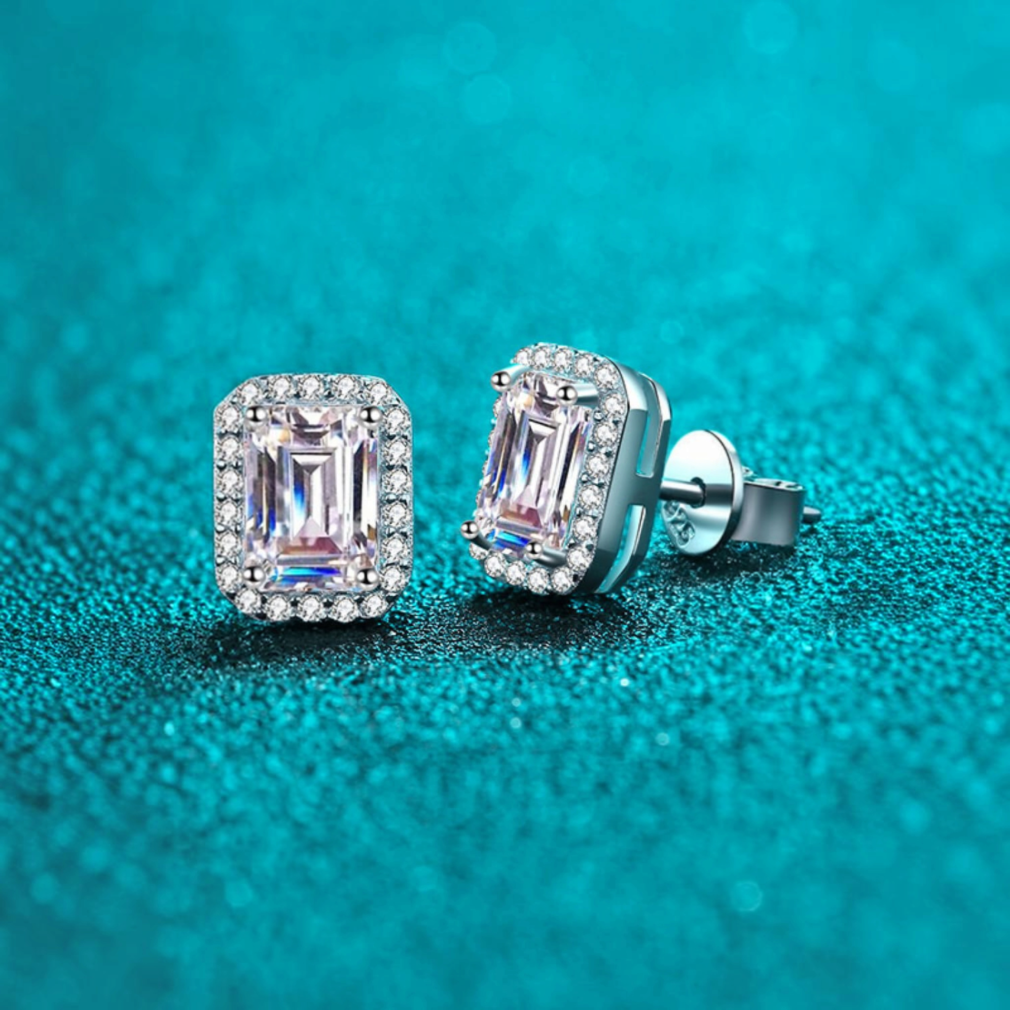 Beach Rose Co. rectangular moissanite halo stud earrings in rhodium-plated sterling silver on a blue glitter surface.