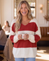 Beach Rose Co. red and cream wide stripe V-neck sweater with dropped shoulders worn by a smiling woman in a cafe