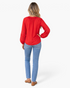 Beach Rose Co. red blouse with long billowy sleeves and crochet openwork panels worn with blue jeans, back view.