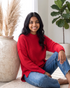 Beach Rose Co. red relaxed knit sweater with exposed seams and dropped shoulders worn by a smiling woman with jeans.