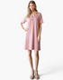 Model wearing a Beach Rose Co. rose pink ribbed A-line t-shirt dress with button-neck detail and side pockets.
