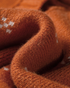 Close-up of Beach Rose Co. rust cardigan fabric with small white knit motifs and soft ribbed texture