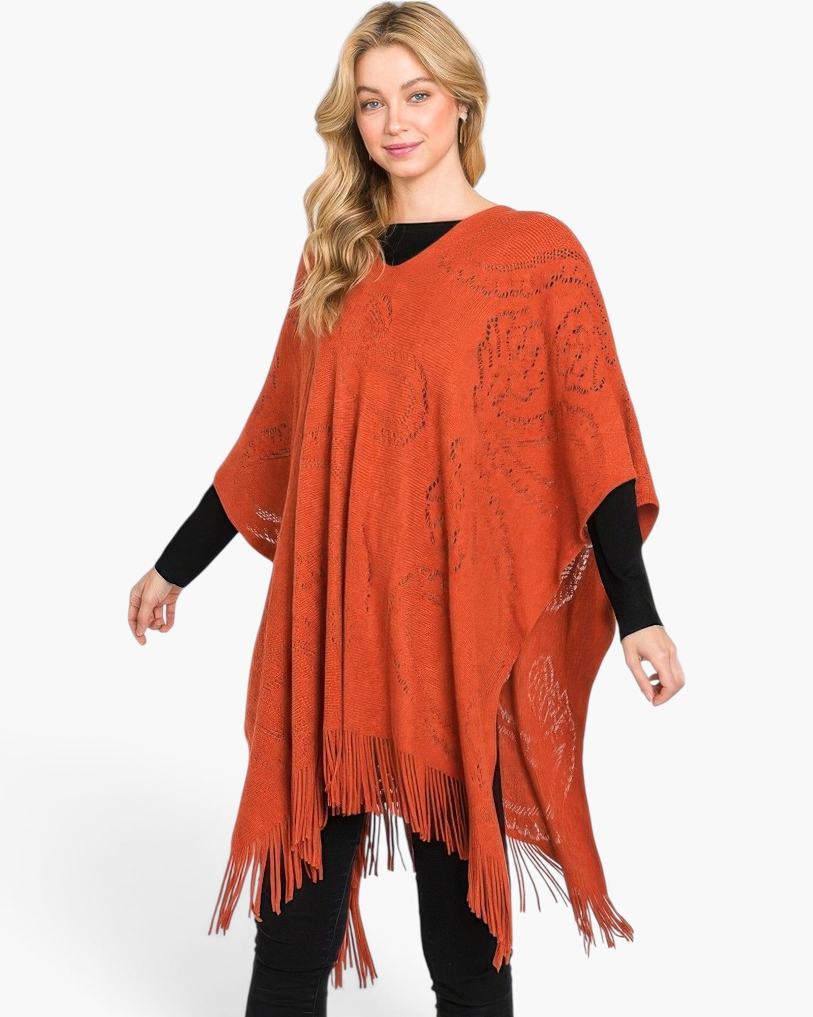 Beach Rose Co. model wearing a rust orange acrylic paisley pattern poncho with a fringe hem over a black long sleeve.
