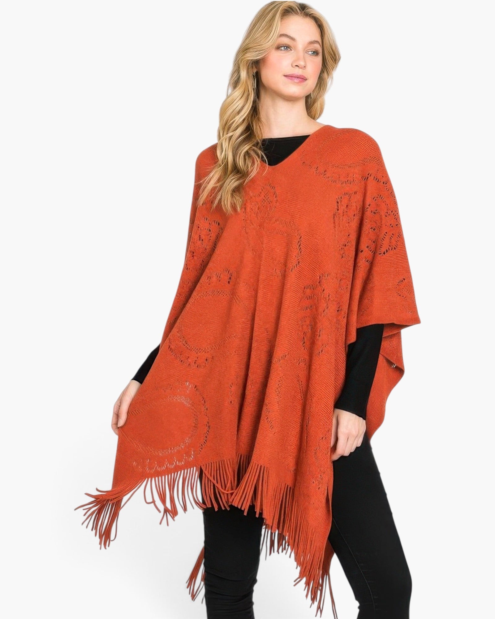 Beach Rose Co. model wearing a rust-orange acrylic paisley pattern poncho with a fringe hem over a black outfit.