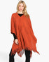 Beach Rose Co. model wearing a rust orange acrylic poncho with a paisley pattern and fringe hem over black clothing.