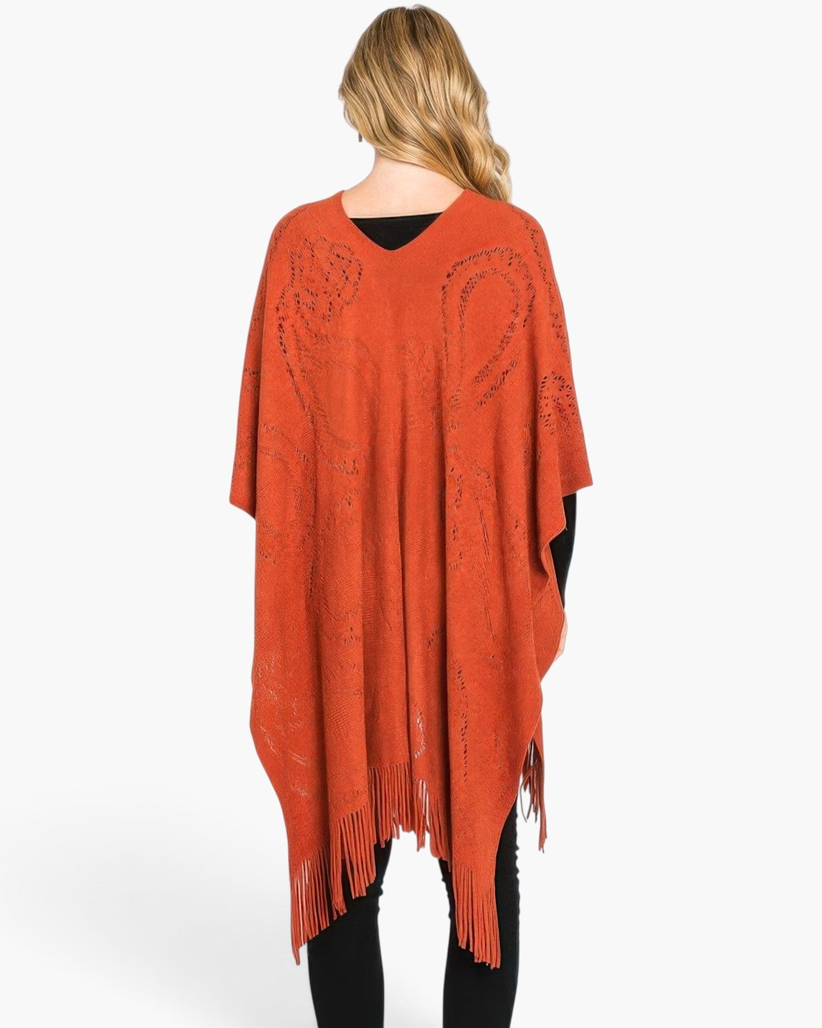 Beach Rose Co. rust orange acrylic poncho with a subtle paisley pattern and fringe hem worn by a woman from behind