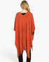 Beach Rose Co. rust orange acrylic poncho with a subtle paisley pattern and fringe hem worn by a woman from behind