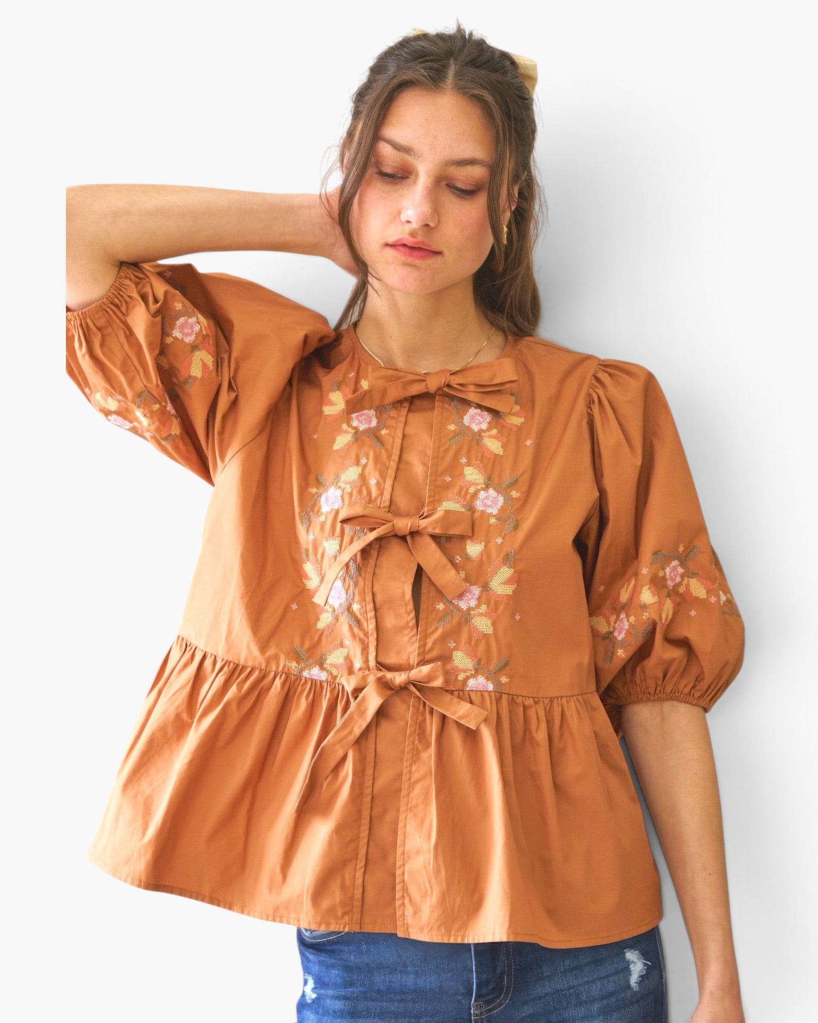 Beach Rose Co. rust-colored poplin blouse with floral embroidery, front ribbon ties, and puff sleeves on a model.