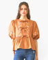 Beach Rose Co. rust-coloured poplin blouse with front ribbon ties, floral embroidery, and puff sleeves on a model.