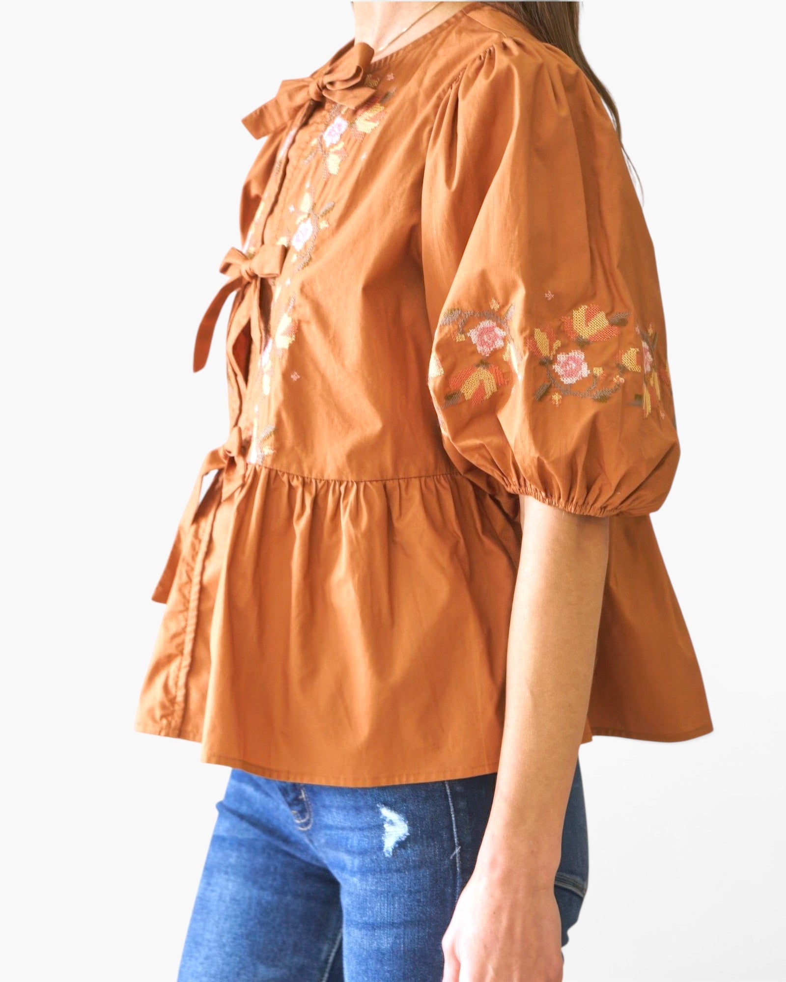 Beach Rose Co. rust-colored poplin blouse with front ribbon ties, puff sleeves, and delicate floral embroidery.