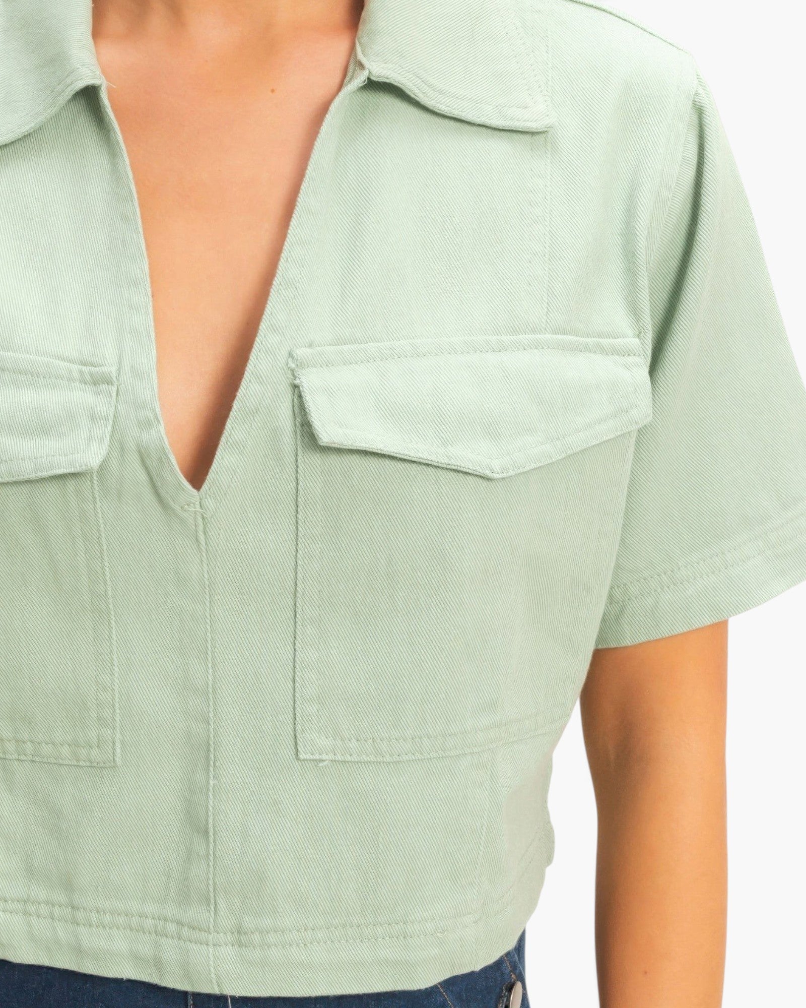 Beach Rose Co. sage green cotton cropped top with a structured collar, deep V-neckline, and two front flap pockets.