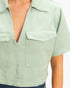 Beach Rose Co. sage green cotton cropped top with a structured collar, deep V-neckline, and two front flap pockets.