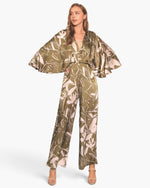 Beach Rose Co. Dreaming Lily satin cape jumpsuit in olive green with a floral print and dramatic flowing sleeves.