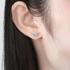 Beach Rose Co. silver starburst moissanite stud earrings worn on an ear, featuring round stones and heart-shaped prongs.