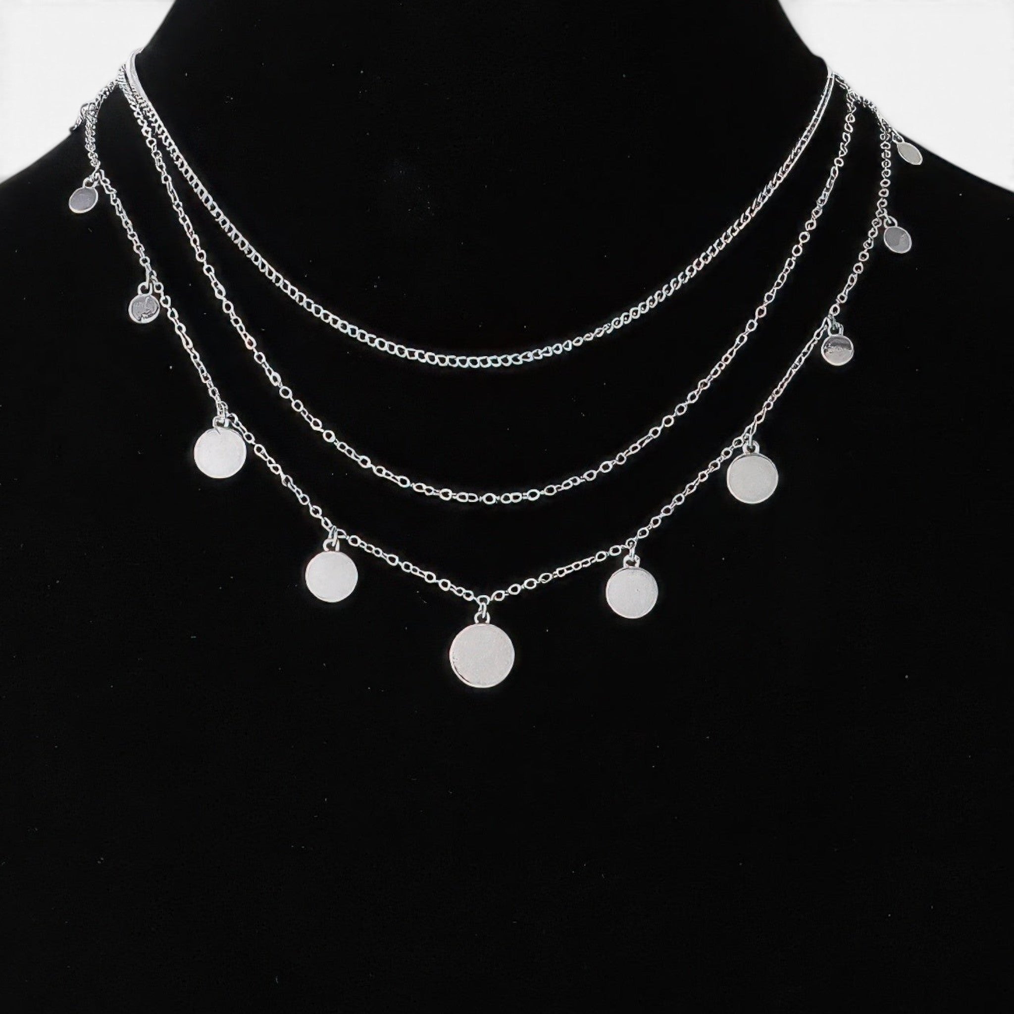 Beach Rose Co. silver triple layered chain necklace featuring delicate round charms on a black display bust.