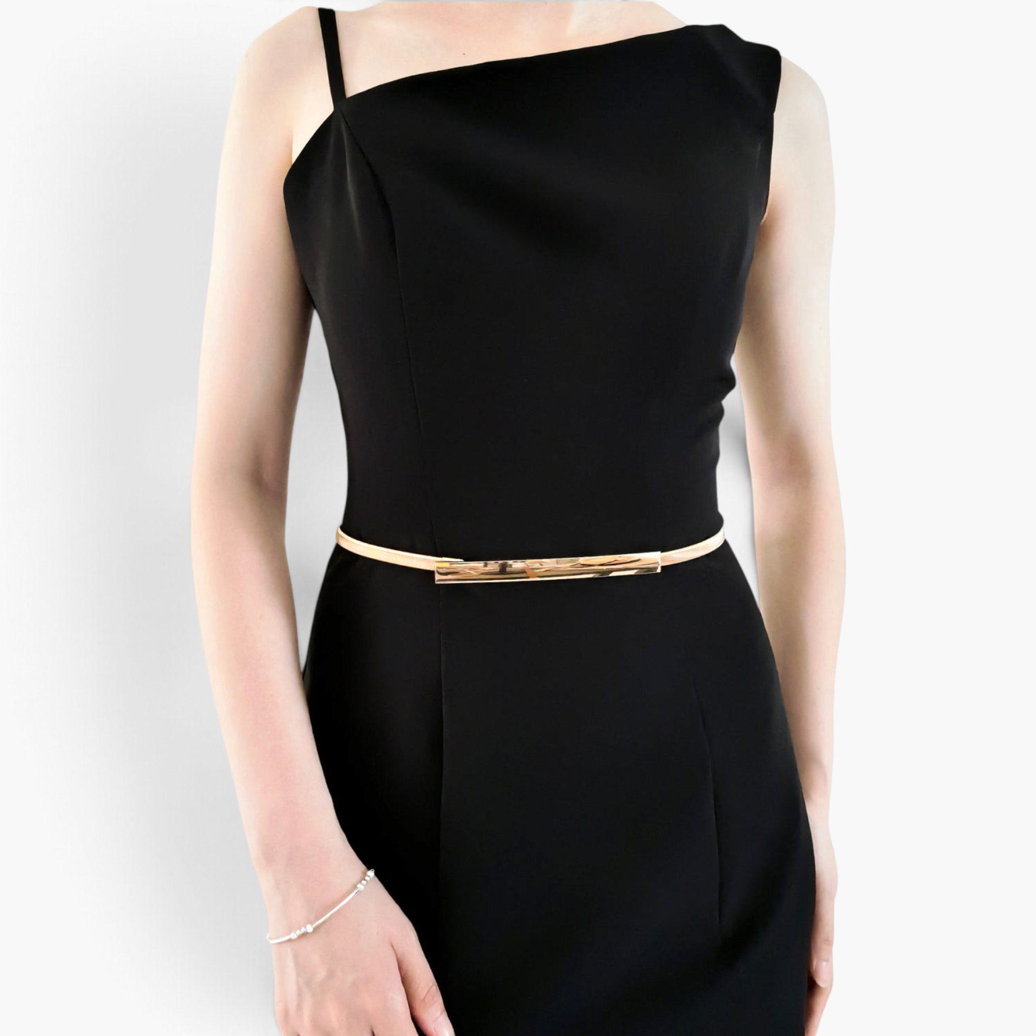 Beach Rose Co. slim gold-toned metal waist belt with a polished rectangular clasp worn over a black dress.