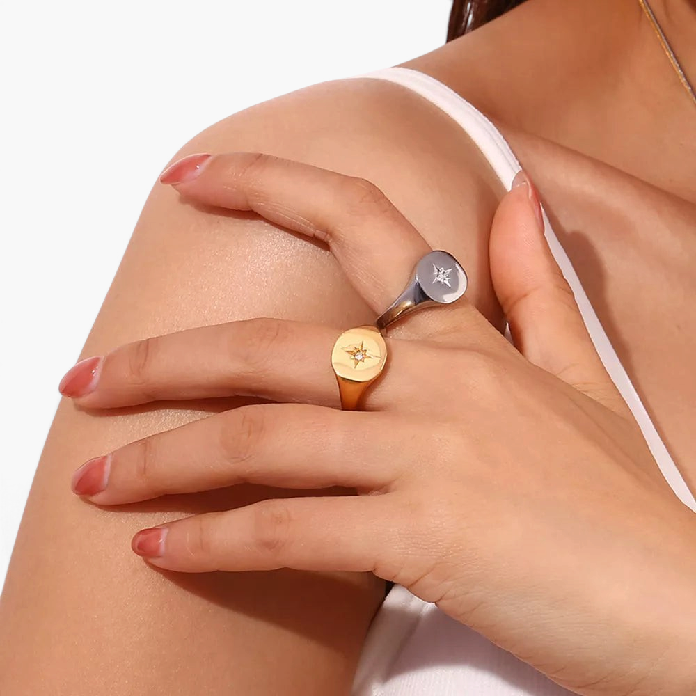 Beach Rose Co. gold and silver signet rings with engraved starbursts and zircon stones worn on a model's hand.