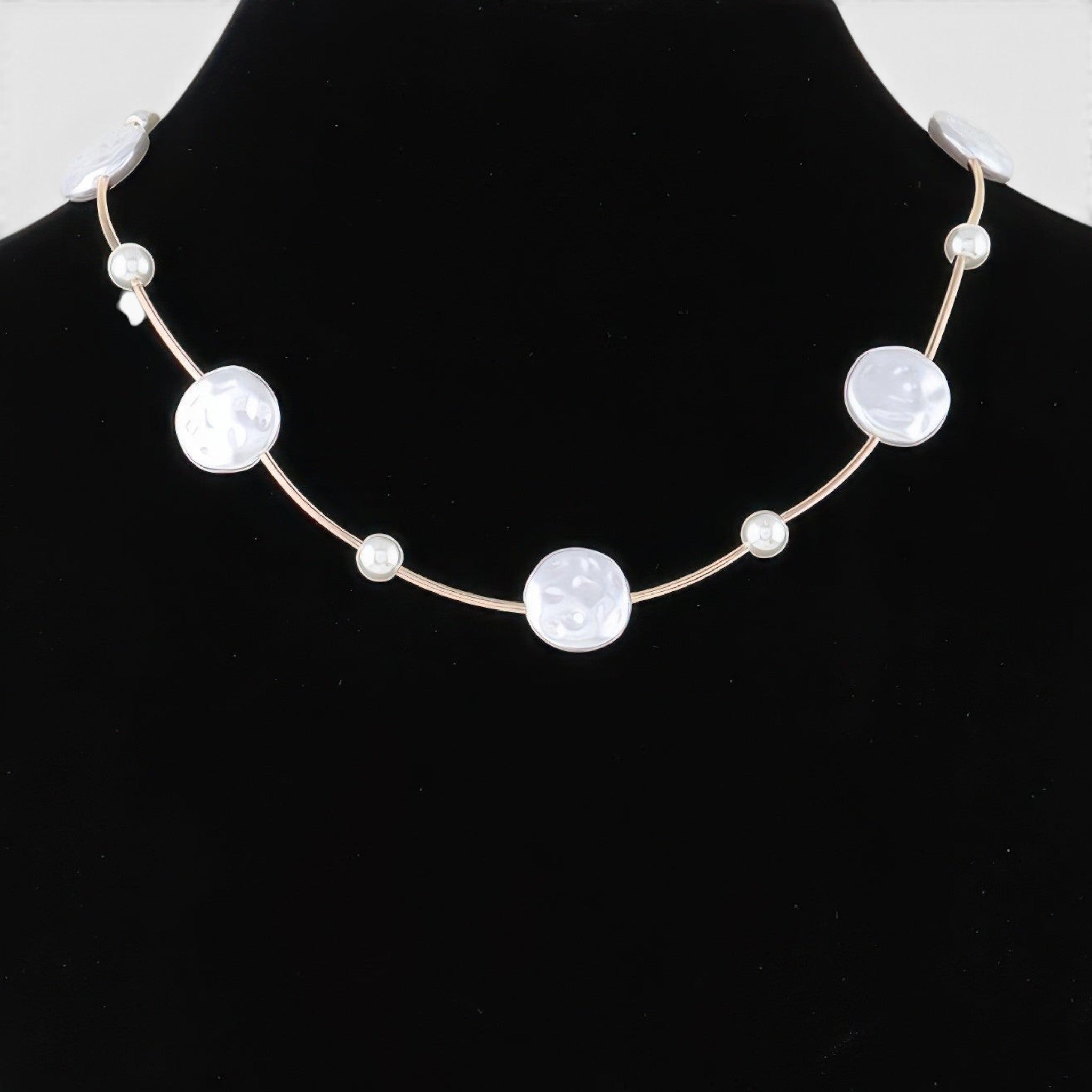 Beach Rose Co. gold cream necklace featuring polished stone beads and delicate charms on a black display bust