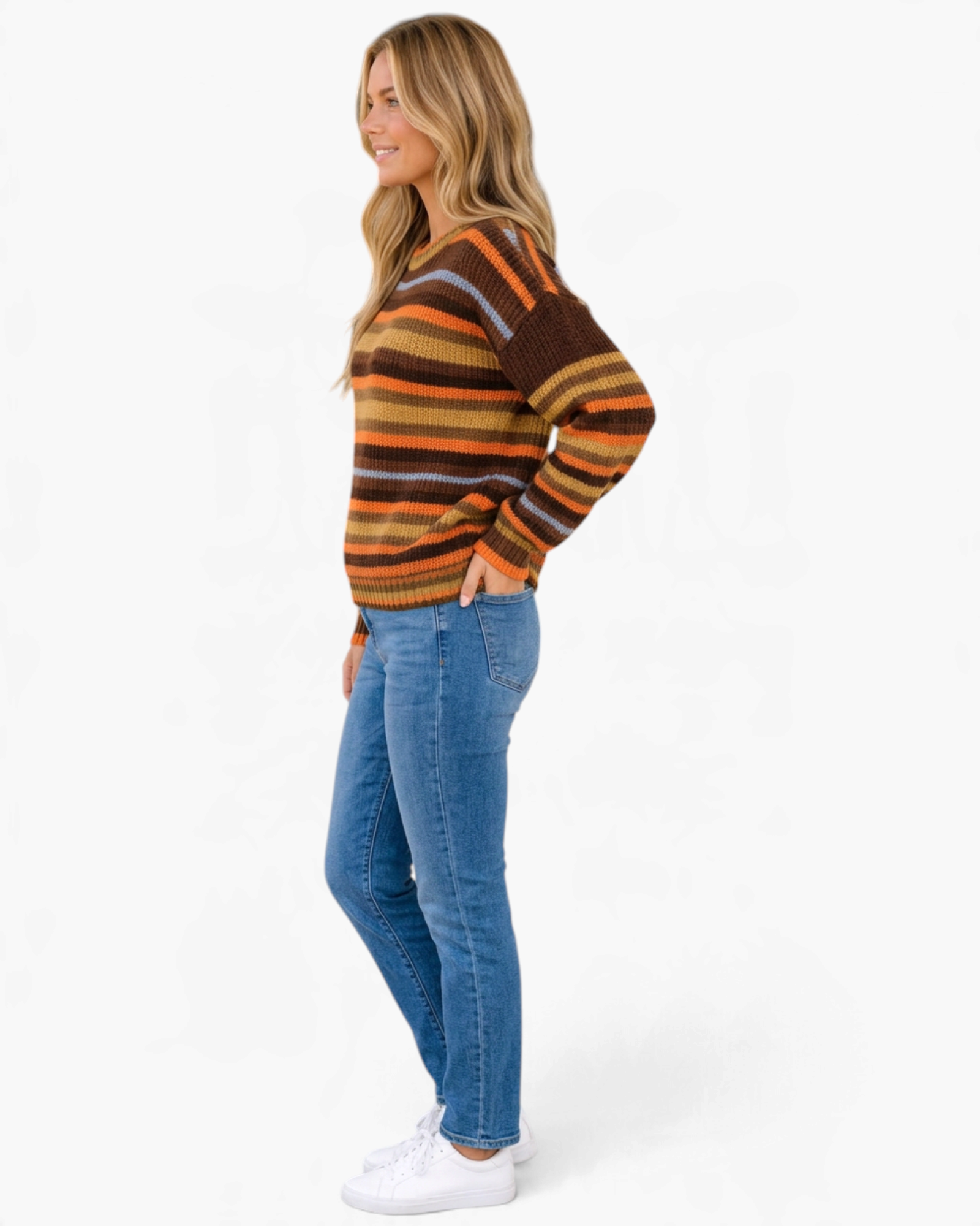 Beach Rose Co. model wearing a brown and orange striped textured knit crewneck sweater with jeans and white sneakers.