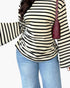 A person wearing a cream and black horizontally striped long-sleeve top with blue jeans, carrying a small burgundy shoulder bag against a plain white background.