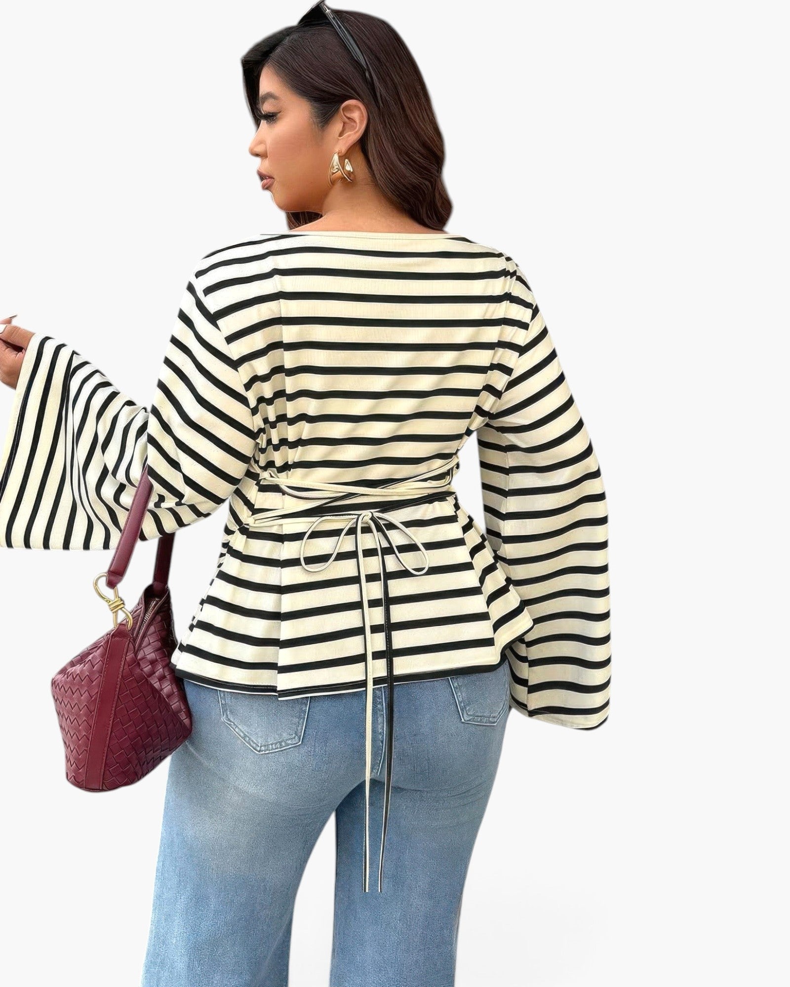 A woman shown from the back wearing a cream and black horizontally striped long-sleeve top with a drawstring waist, paired with light blue jeans and carrying a dark red textured handbag, against a plain white background.