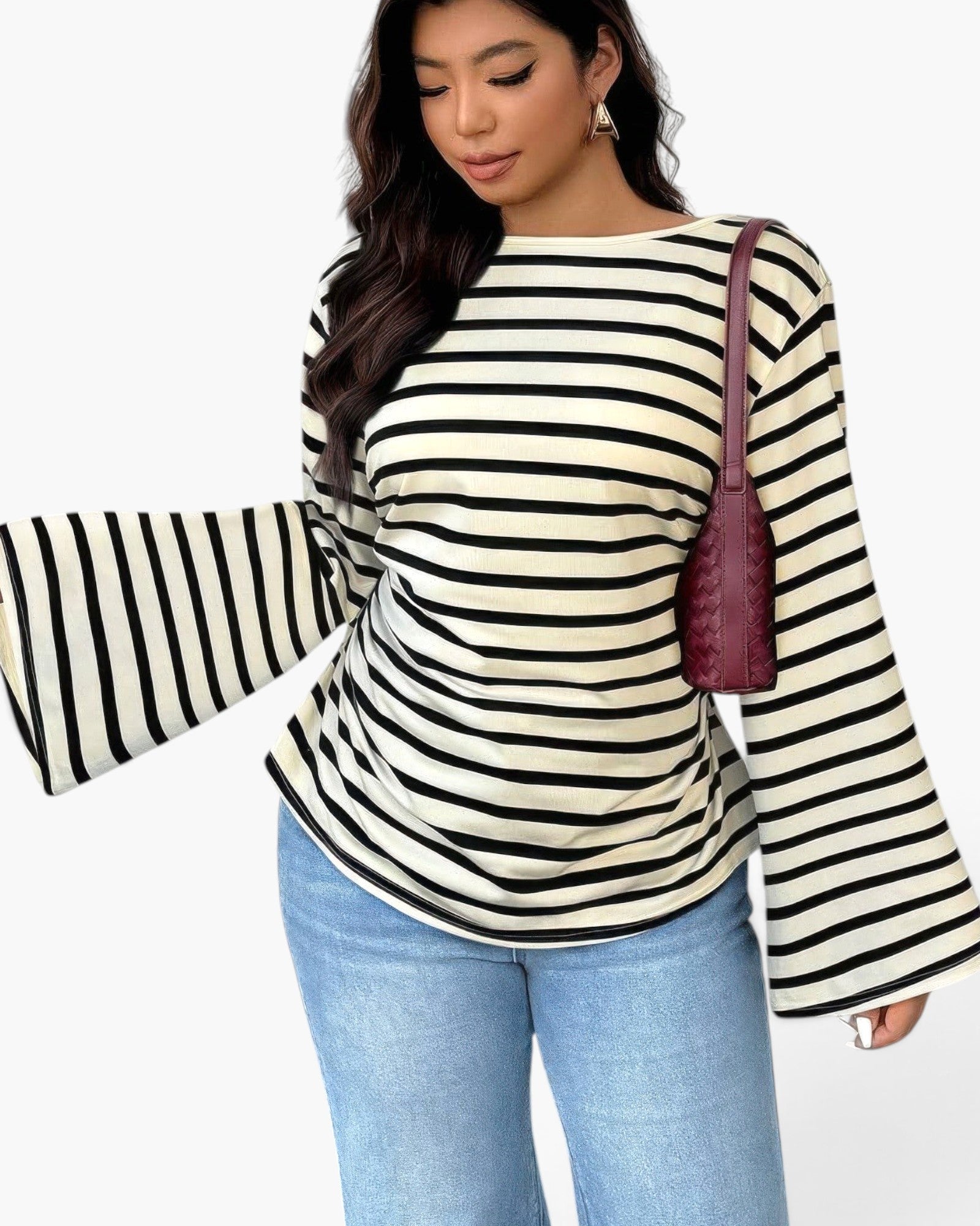 A woman wearing a cream and black horizontally striped long-sleeve top with flared bell sleeves, paired with light blue jeans and a dark burgundy shoulder bag, against a plain white background.