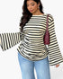 A woman wearing a cream and black horizontally striped long-sleeve top with flared bell sleeves, paired with light blue jeans and a dark burgundy shoulder bag, against a plain white background.