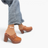 Beach Rose Co. tan leather platform clogs with silver studs, buckle detail, and chunky block heels on a model.