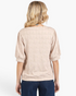 Back view of Beach Rose Co. tan textured top with puff sleeves and banded hem worn with blue jeans