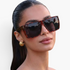 Beach Rose Co. oversized flat-top square sunglasses in tortoiseshell print worn by a woman with gold hoop earrings.