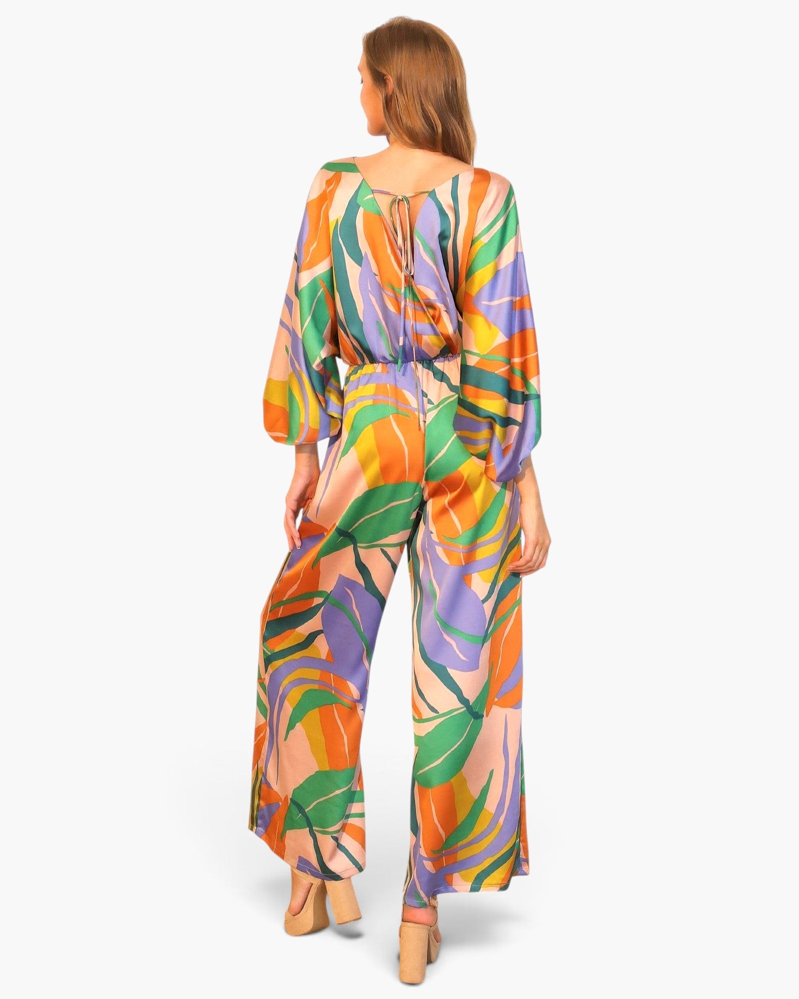 Back view of a model wearing a Beach Rose Co. satin jumpsuit with a vibrant tropical print and blouson bodice.