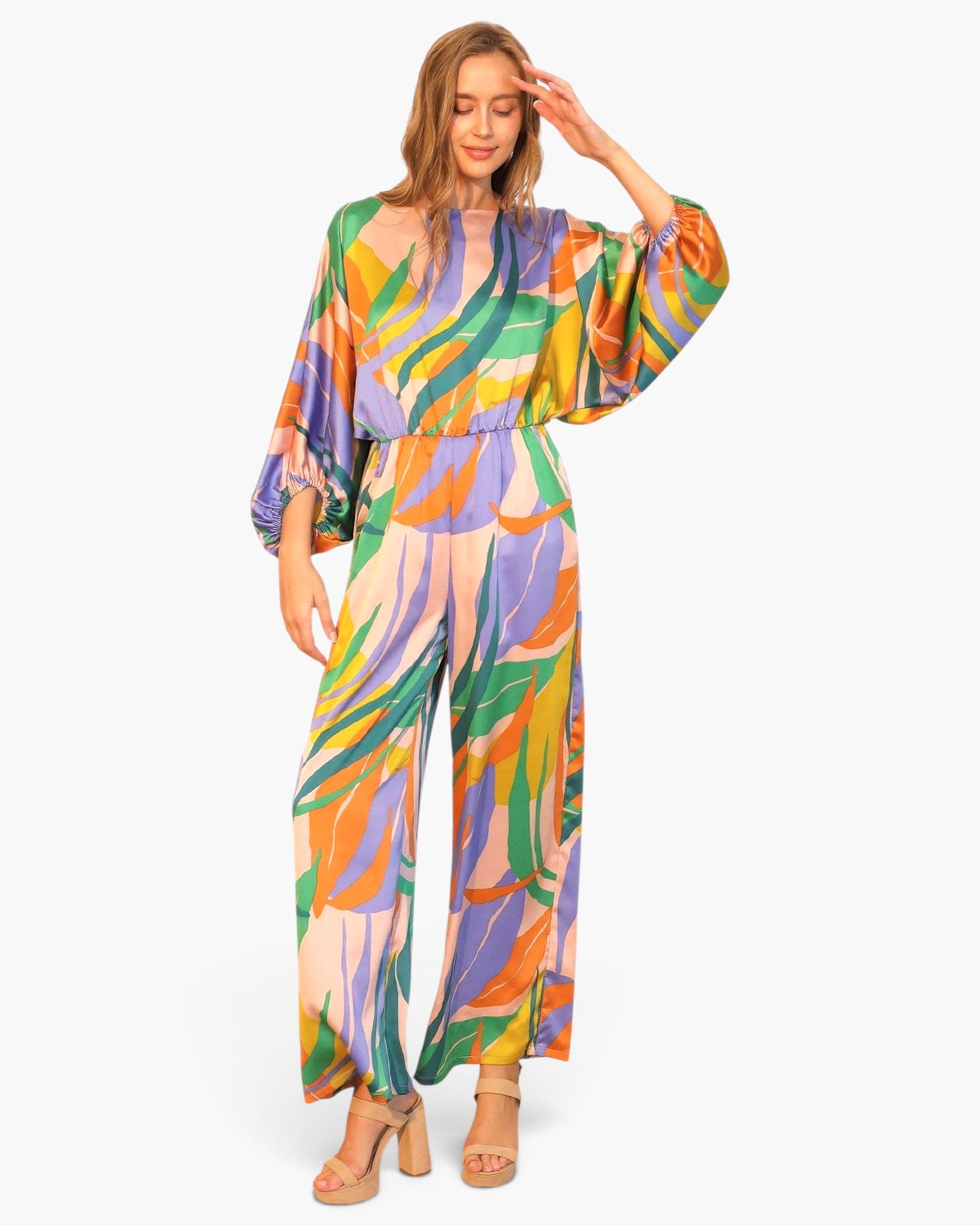 Model wearing Beach Rose Co. Isla Tropical satin jumpsuit with boat neck, blouson sleeves, and vibrant leaf print.