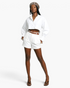 Beach Rose Co. white cropped blouse with balloon sleeves, smocked cuffs, and button front worn with white shorts.